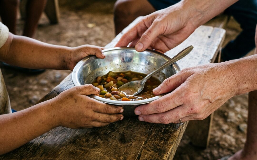 Donor kneeling beside a child at a Honduras feeding center, both looking at a bowl of food in natural light.