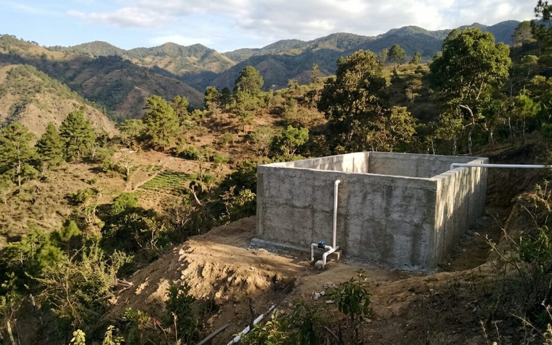 Donor and local community leader standing together beside a completed water cistern in the mountains of Honduras at dusk.